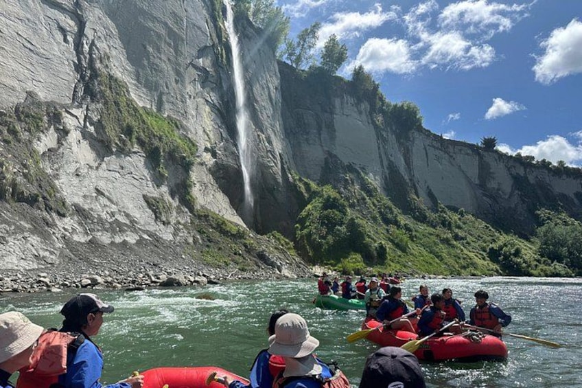 A group of people rafting down a river with a waterfall in the background. 2