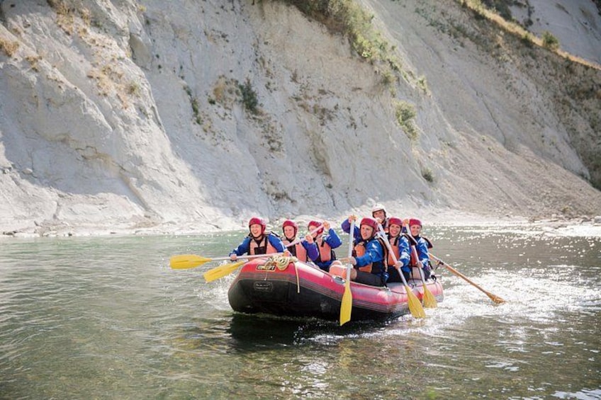 A group of people in a raft navigating a river with rocky cliffs in the background. 5