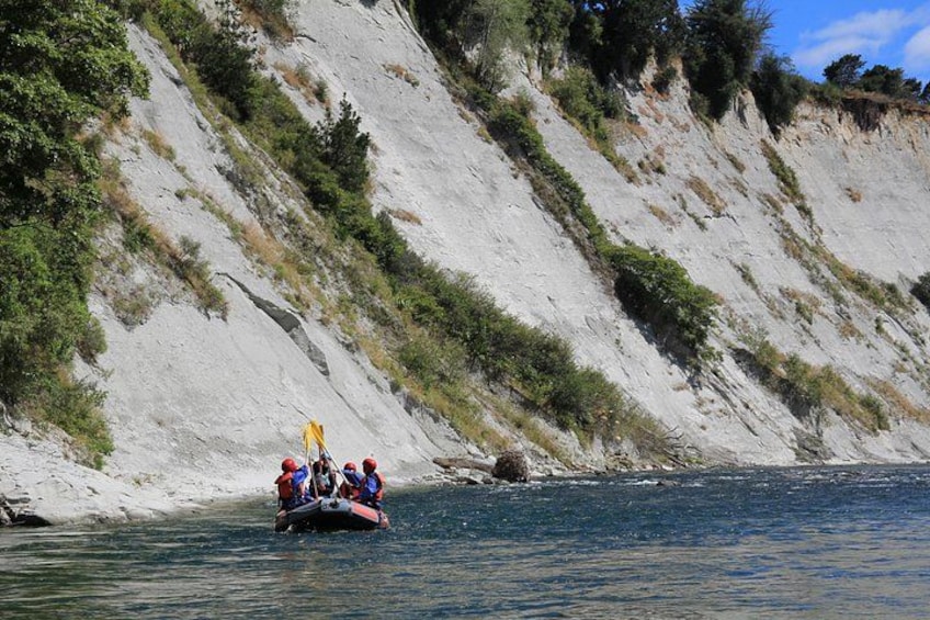 A group of people in a raft on a river, surrounded by steep, rocky cliffs. 4
