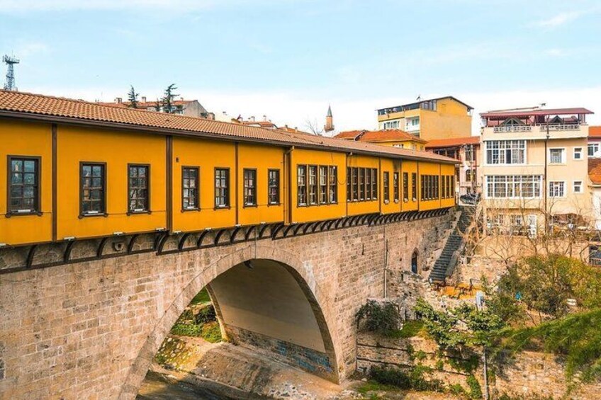A yellow building with a stone bridge arching over a river. 5