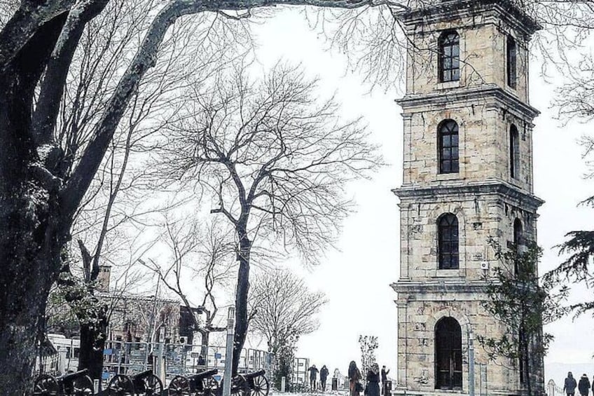 A historic stone tower with multiple levels, surrounded by leafless trees and a crowd of people. 3