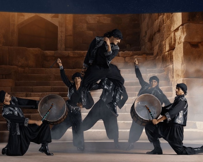 A group of people in black attire performing an energetic dance with drums in an ancient stone structure. 2