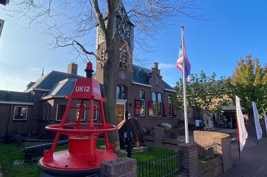 Un hidrante rojo con la etiqueta 'UK12' frente a un edificio histórico con una torre de reloj. 2