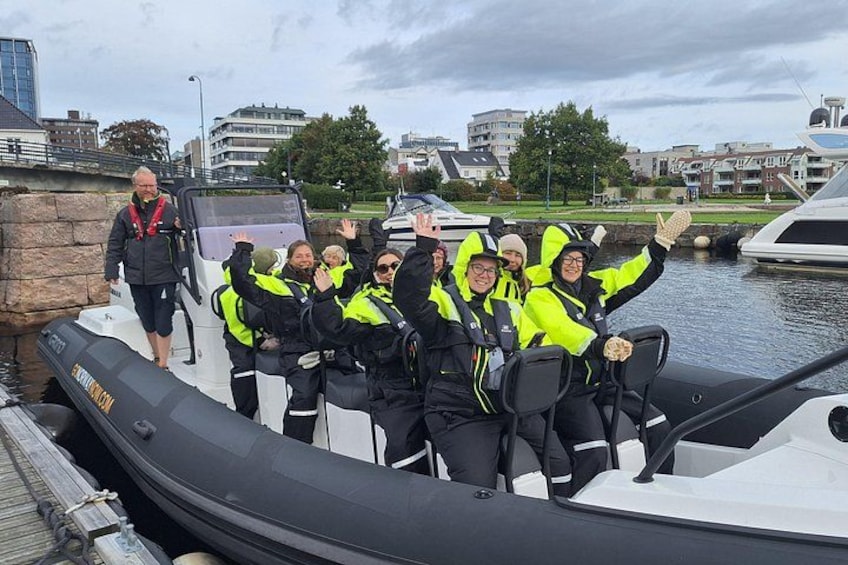 A group of people on a boat wearing life jackets, with a cityscape in the background. 3