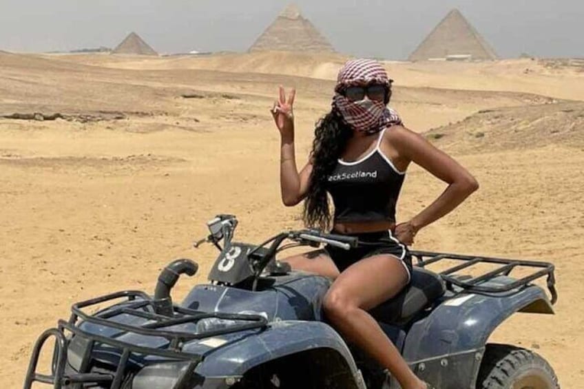 A person on an ATV in a desert with pyramids in the background. 5