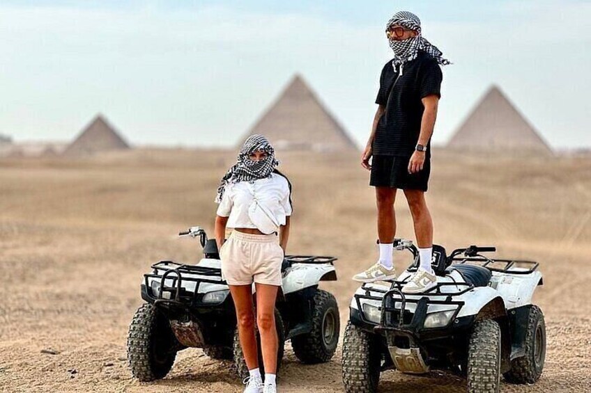 Two people on ATVs in a desert with pyramids in the background. 3