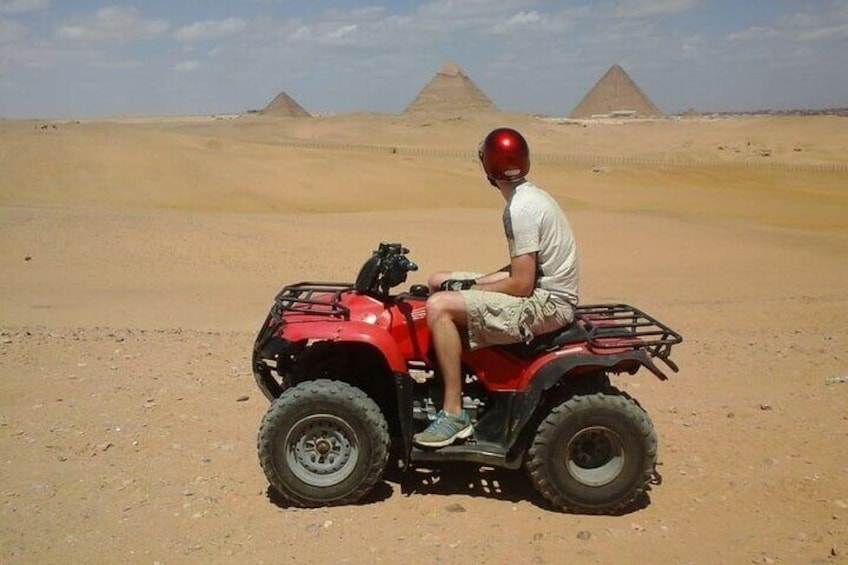 A person on a red ATV in a desert with pyramids in the background. 1