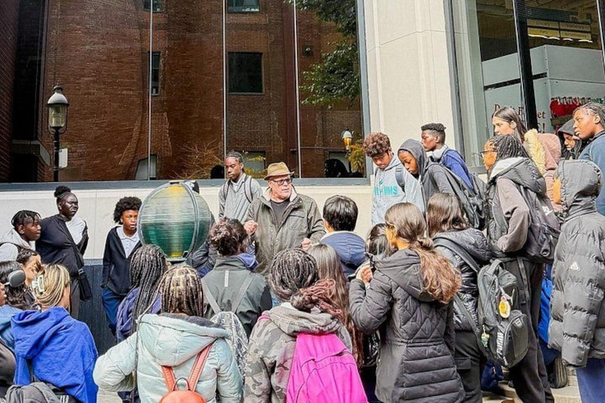 A group of people standing in a circle outdoors, some wearing winter clothing. 1