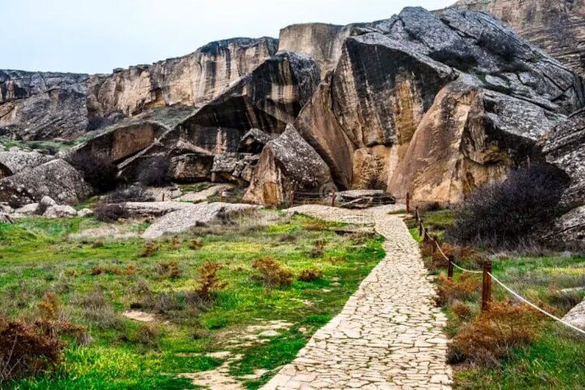 A stone pathway leading through a rocky landscape with large boulders and sparse vegetation. 1