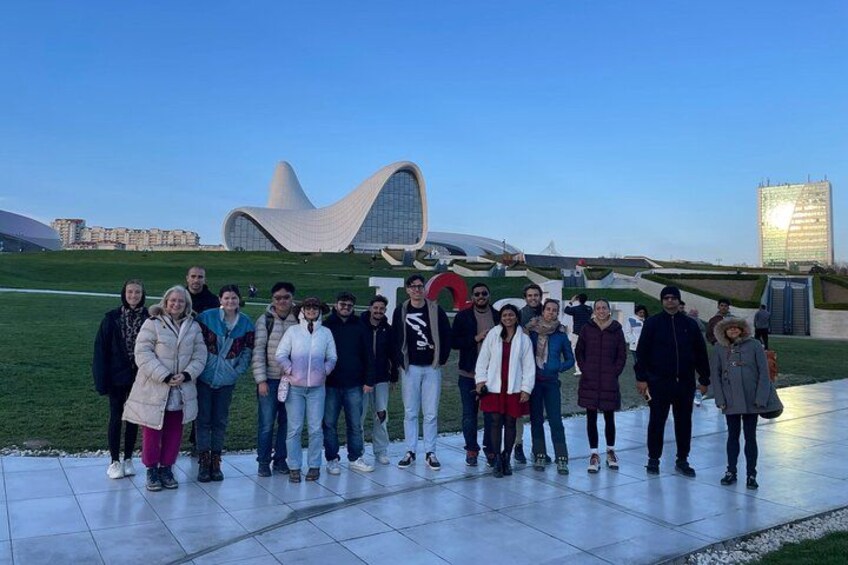 A group of people standing in a line on a paved area with a modern building in the background. 4