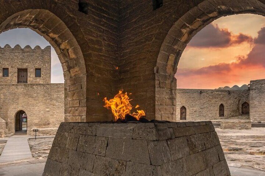Estructura de piedra con arcos, un fuego encendido en el centro y una puesta de sol al fondo. 4