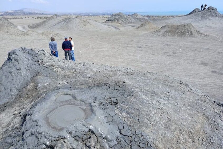A barren landscape with a large crater and people standing on a mound in the distance. 2