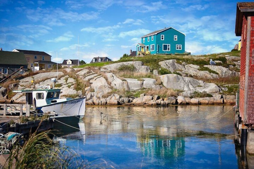 A coastal scene with a house on a rocky hill, a boat docked at a pier, and calm water reflecting the sky. 2