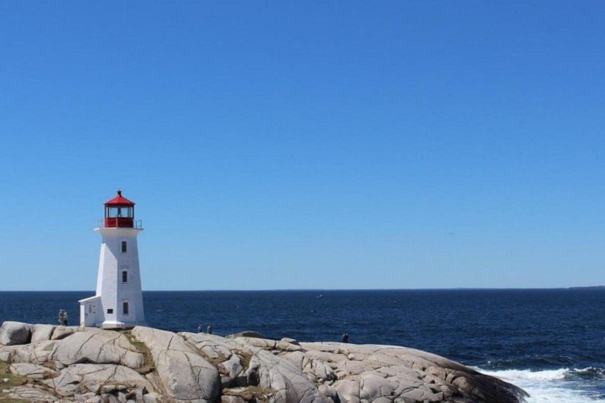 A white lighthouse with a red top on a rocky outcrop by the sea. 2