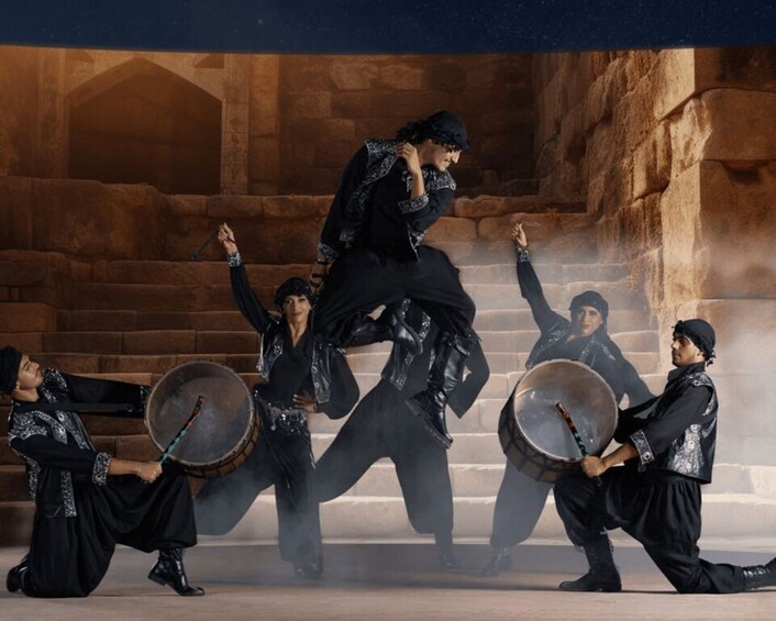A group of performers in black attire with drums, performing in an ancient stone structure. 5