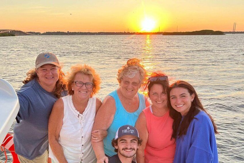 A group of people on a boat with a sunset in the background. 2