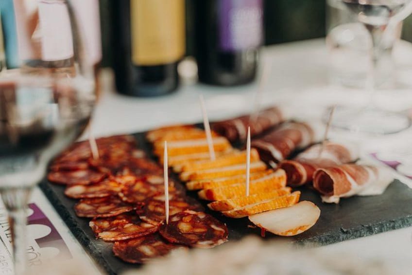 Un tagliere con salumi e formaggi assortiti, accompagnato da bicchieri di vino. 2