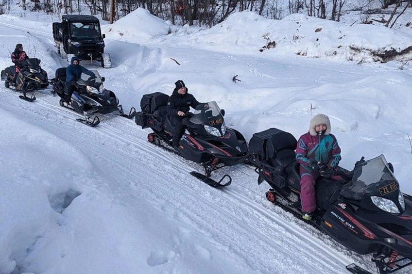 En gruppe mennesker på sne-scootere på en sneklædt skråning. 1