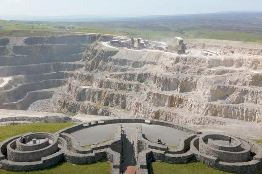 Een grote, ronde stenen structuur met concentrische ringen, omgeven door terrasvormige heuvels. 3