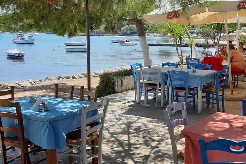 A seaside restaurant with outdoor seating, boats on the water, and a clear view of the sea. 4