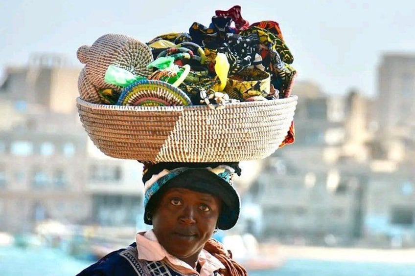 A person carrying a large woven basket filled with colorful items on their head. 4