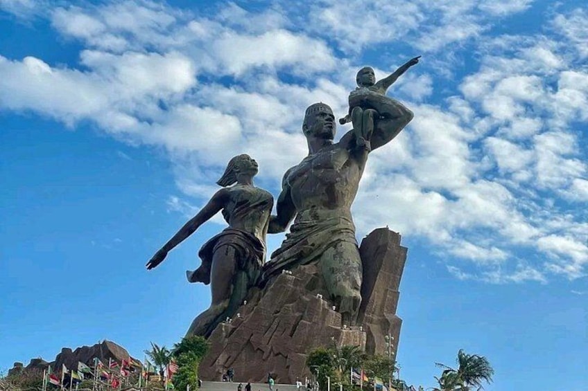 A large statue of a man and woman with a child, set against a clear blue sky with clouds. 3