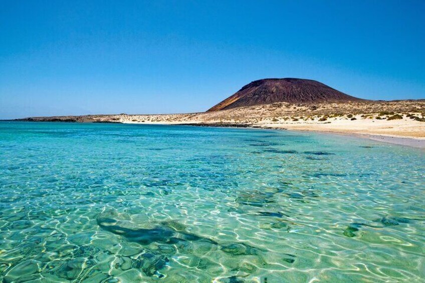 Una playa con agua turquesa cristalina y una montaña al fondo. 2