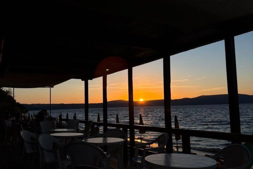 A sunset view from a covered outdoor seating area with tables and chairs. 2