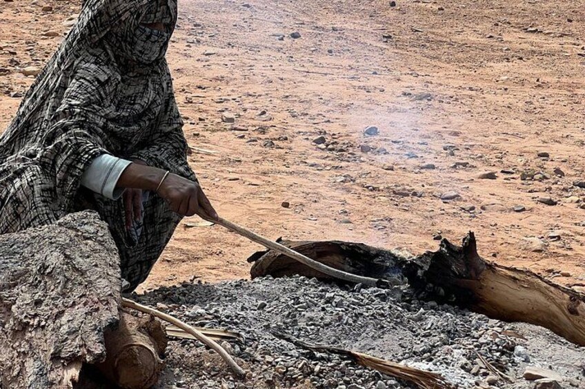 A person sitting on the ground, surrounded by rocks and charred wood, possibly engaged in a traditional activity. 5