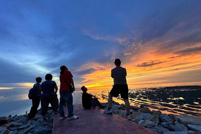 A sunset over a rocky shoreline with people standing and sitting on the rocks. 3