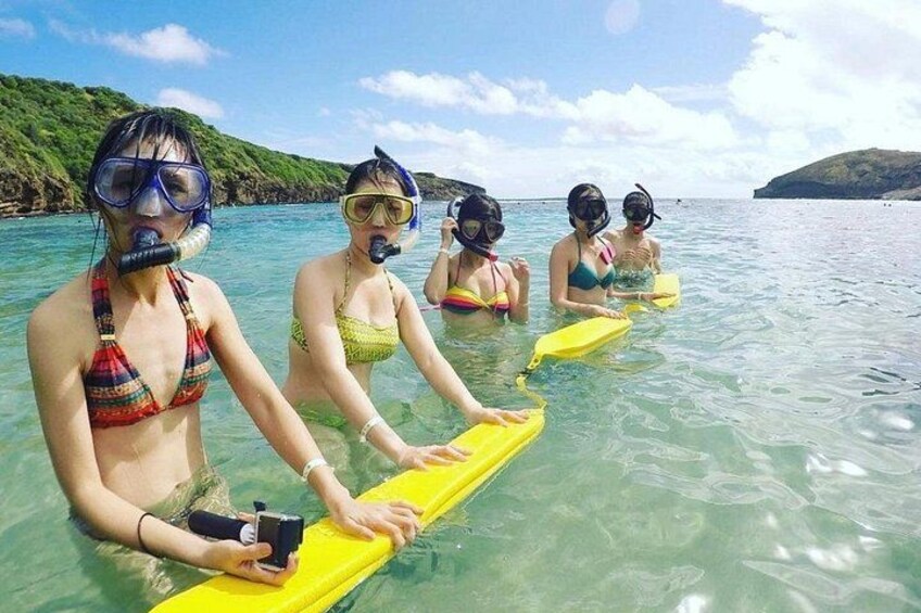 People snorkeling in a clear blue sea with a hilly landscape in the background. 2