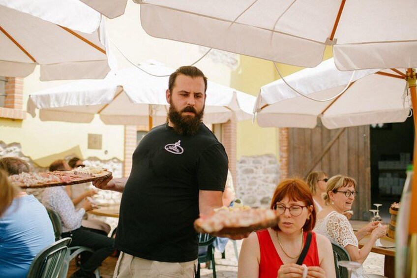 Una persona serve cibo in un'area pranzo all'aperto con ombrelloni bianchi. 3