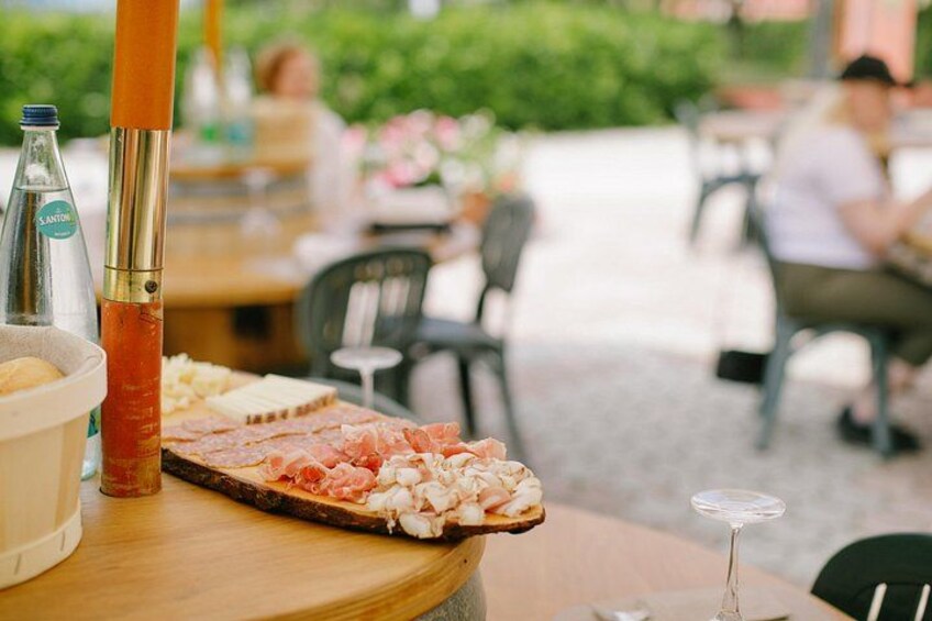 Un tavolo di legno con un tagliere di salumi, una bottiglia di salsa e un bicchiere. 2