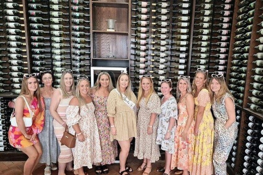 Un grupo de personas frente a una pared de botellas de vino. 5