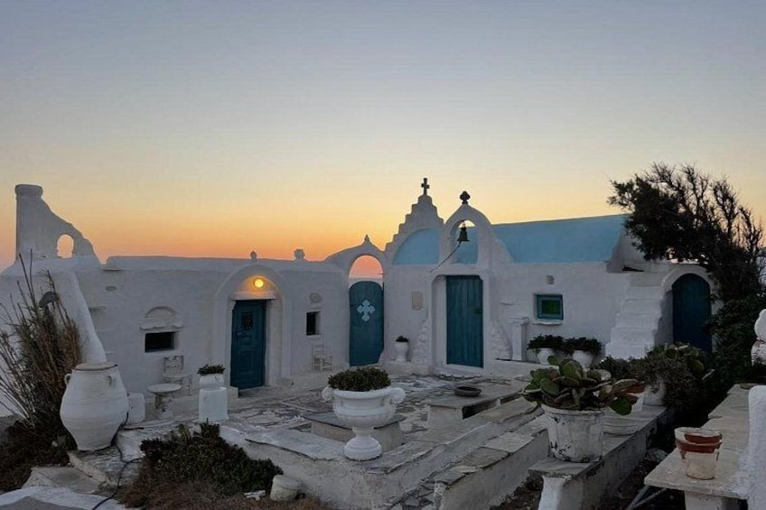 A white building with blue doors and windows, surrounded by potted plants and a sunset sky. 2