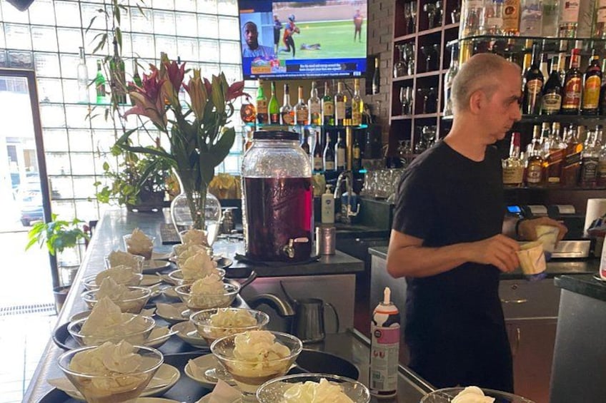 A bar with a bartender, a large jar of liquor, and a TV screen in the background. 3