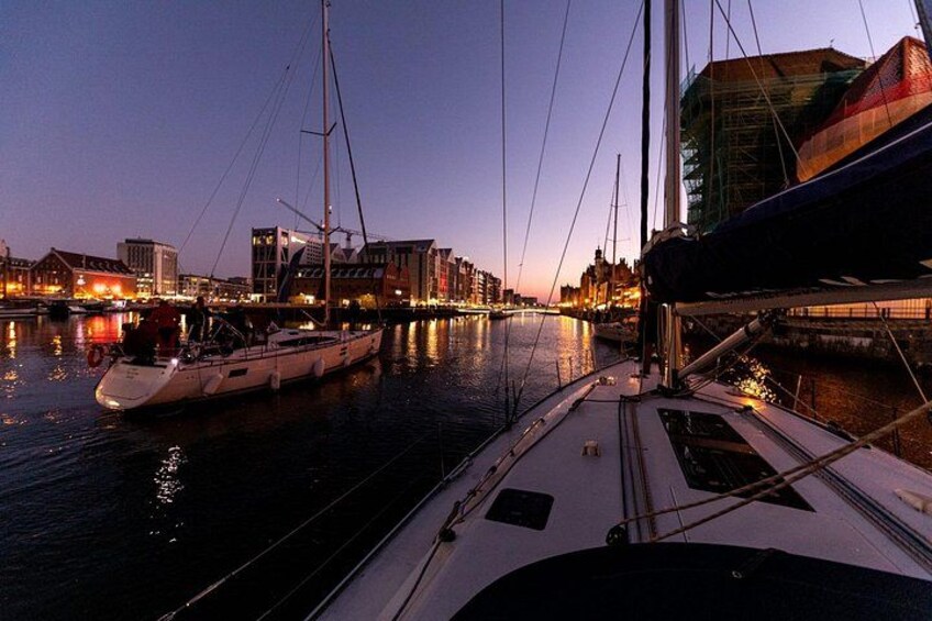 Een jachthaven in de schemering met aangemeerde boten, een stadsachtergrond en een brug over het water. 5