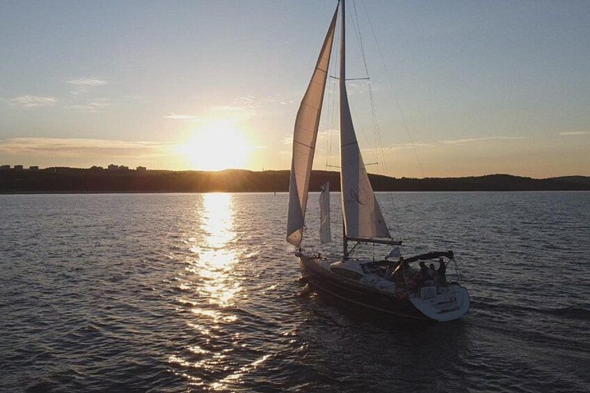 Een zeilboot op rustig water, met een ondergaande zon op de achtergrond. 2
