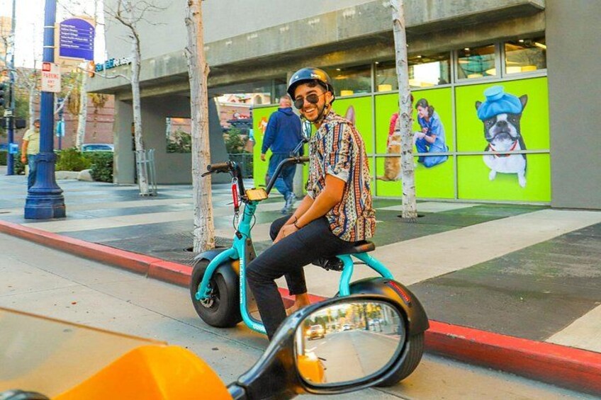 A person riding a teal Segway on a city street with a green wall and a mural in the background. 3