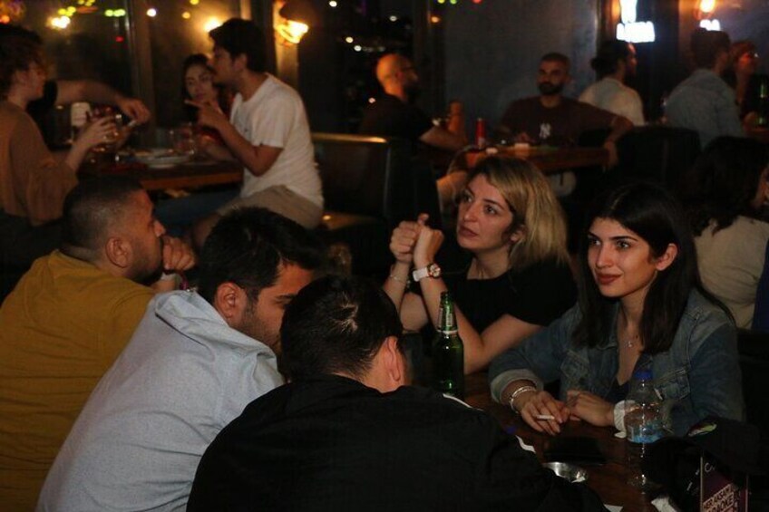 Un bar bondé où les gens sont assis à des tables, certains ayant des verres à la main. 3