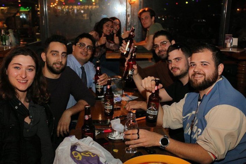 Un gruppo di persone sedute attorno a un tavolo con bottiglie e bicchieri, probabilmente in un bar o ristorante. 2