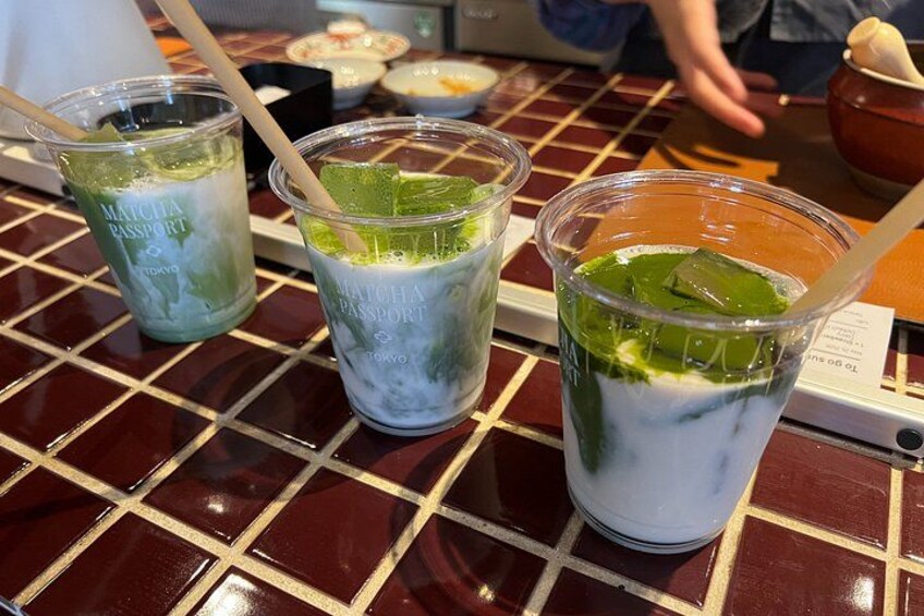 Tres cafés matcha en vasos de plástico transparente con pajitas sobre una mesa con baldosas. 5