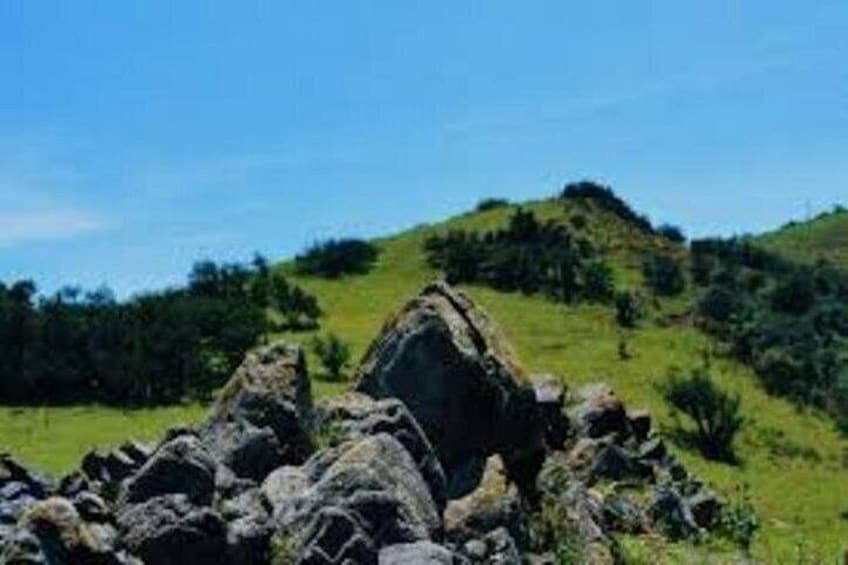 A rocky landscape with a prominent rock formation in the foreground and a hill with sparse vegetation in the background. 1