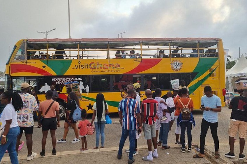 A double-decker bus with 'Visit Ghana' written on it, surrounded by people. 1