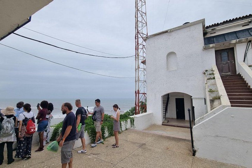 A group of people standing on a terrace overlooking the sea, a white building with a staircase, and a tall communication tower. 4