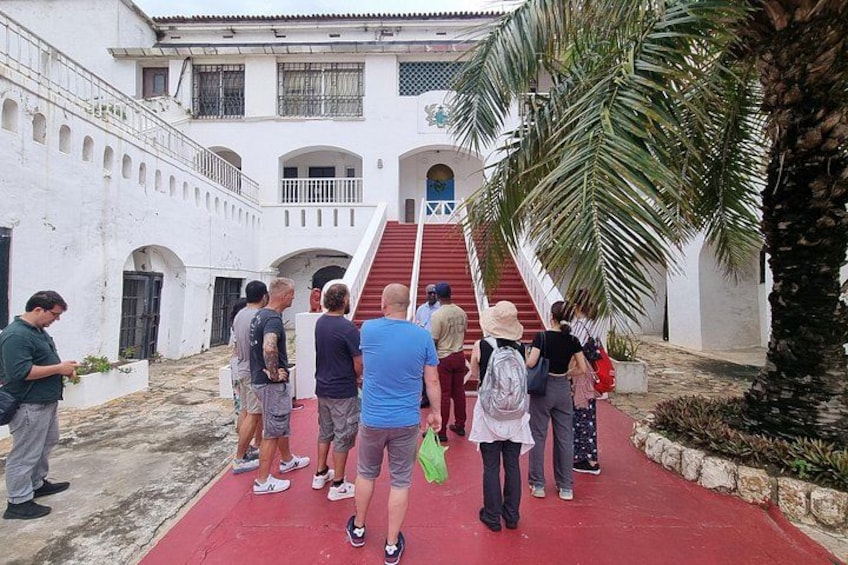 A group of people standing on a red carpet in a courtyard with white walls and a staircase. 5