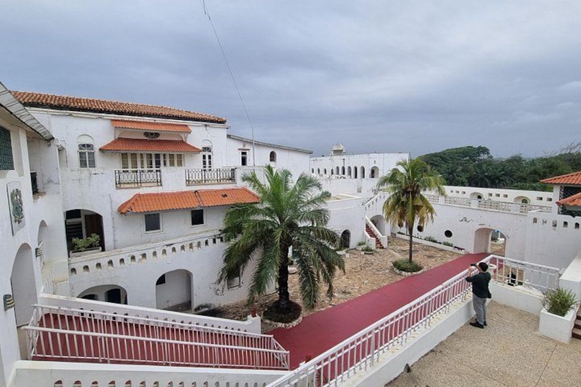 A white building with red-tiled roofs, palm trees, and a red pathway. 3