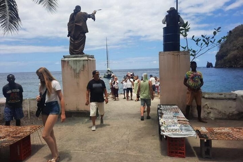 Un paseo marítimo con estatuas, un puesto de mercado y gente caminando. 2