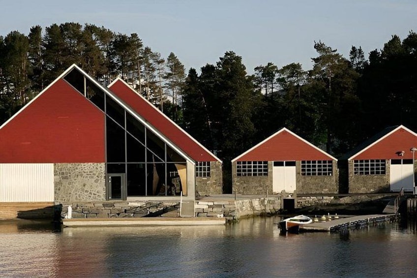 Una serie de edificios con techos rojos y grandes ventanales, ubicados junto a una masa de agua tranquila, con árboles al fondo. 2