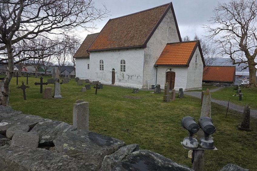 Una iglesia blanca con techo rojo, rodeada por un cementerio con lápidas y un muro de piedra. 3